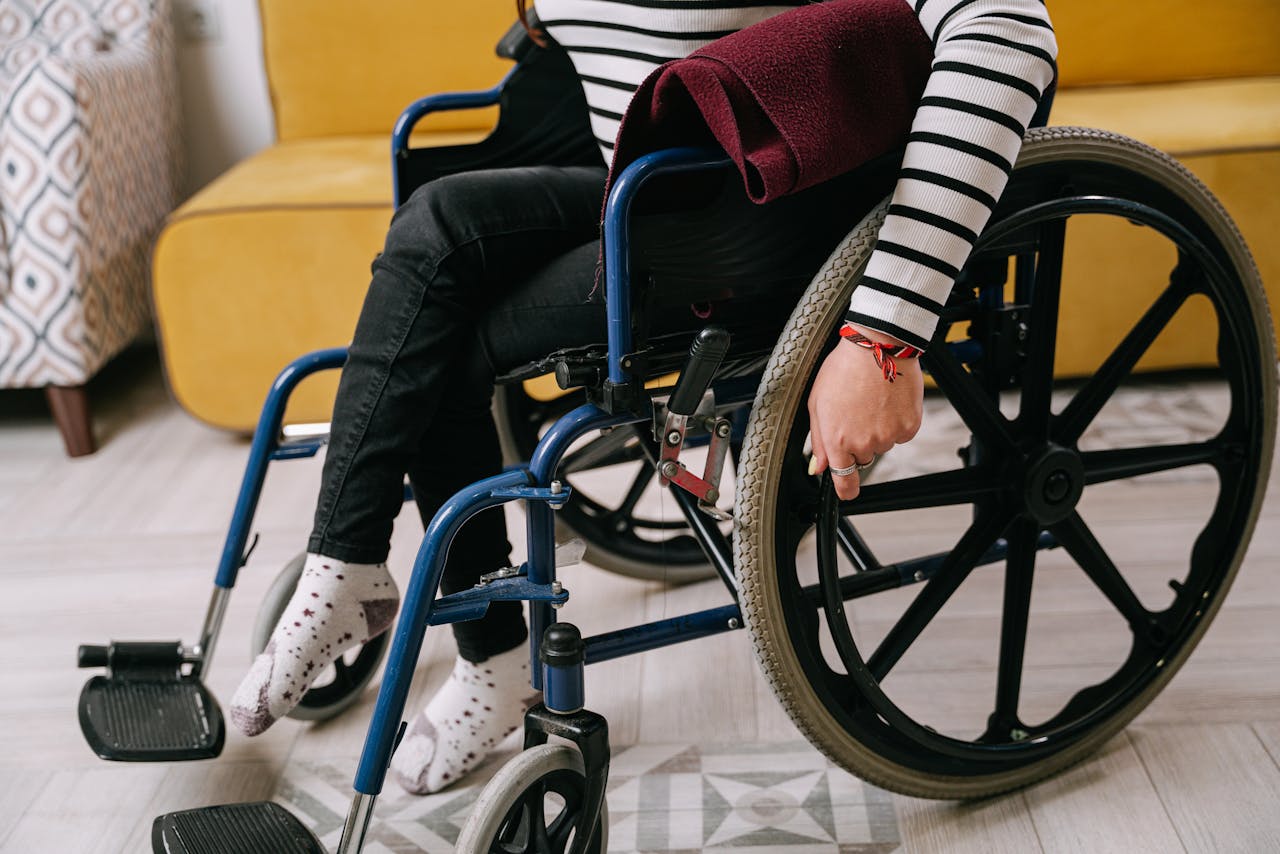 Person sitting in a wheelchair indoors wearing a striped shirt. Cozy and supportive environment.
